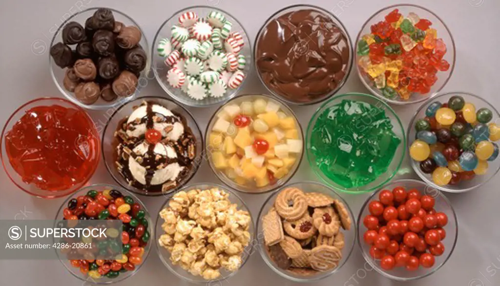 Overhead view of 13 glass bowls of various sweets: pudding, mints, cookies, jell-o, gummi bears, fruit, chocolates to name a few