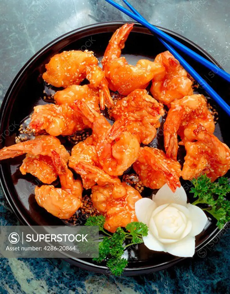Plate of shrimp, fried golden brown with sesame seeds, alongside a sliced radish garnish and blue chopsticks.