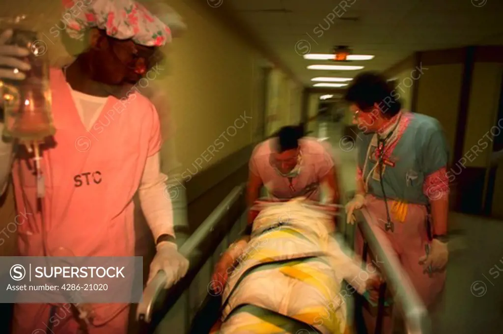 Nurses at UMBC Shock Trauma Center in Baltimore, Maryland taking a patient on gurney down a corridor in hospital.