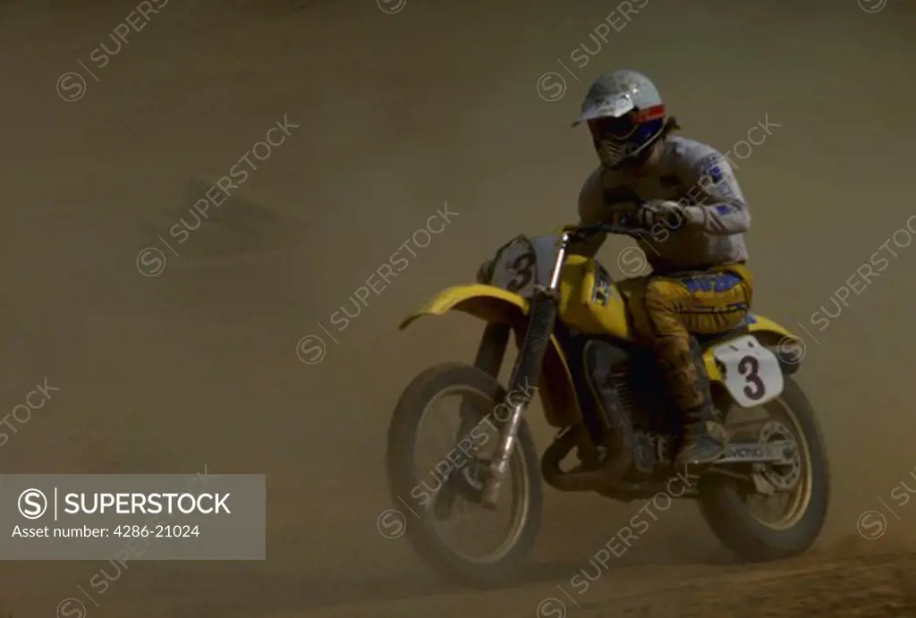 Motorcross racer riding a yellow motorcyle kicking up dust during a race.