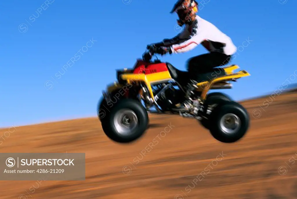 Blurred action shot of yellow four-wheeled ATV in mid-air jump, Hurricane Sand Dunes, southern Utah. 