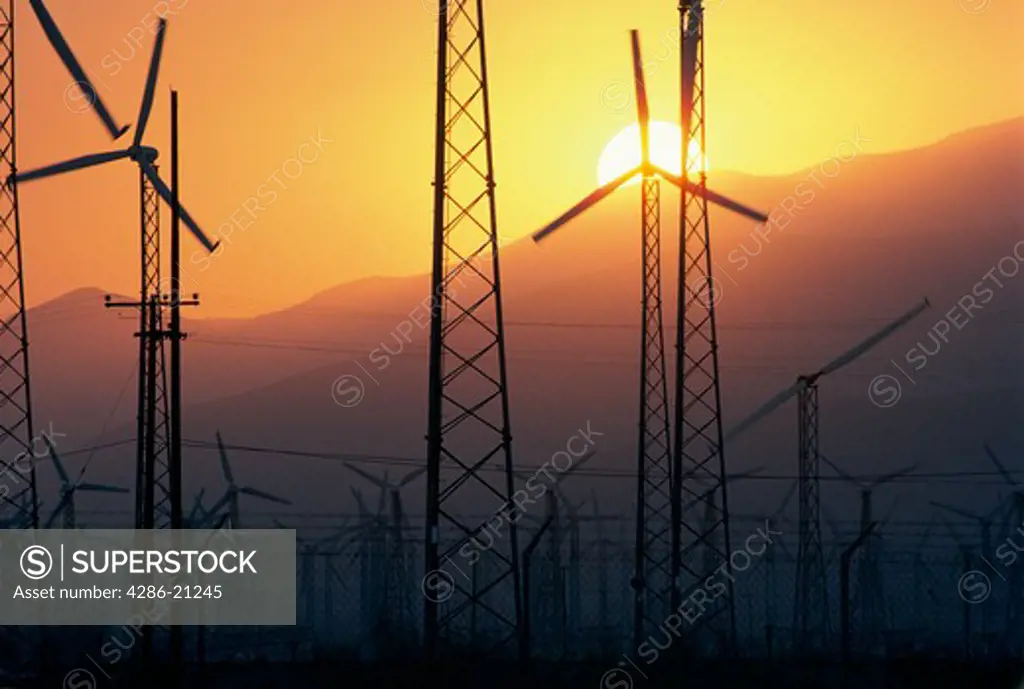 Modern electricity generating windmills silhouetted by the sun setting behind mountains near Palm Springs, California.