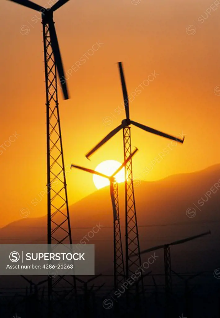 Modern electricity generating windmills silhouetted by the sun setting behind mountains near Palm Springs, California.