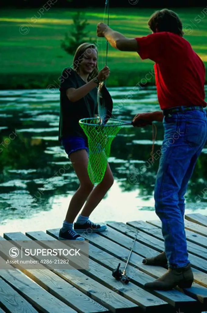 Dad helps daughter net a bass from her rod at farm pond.MR