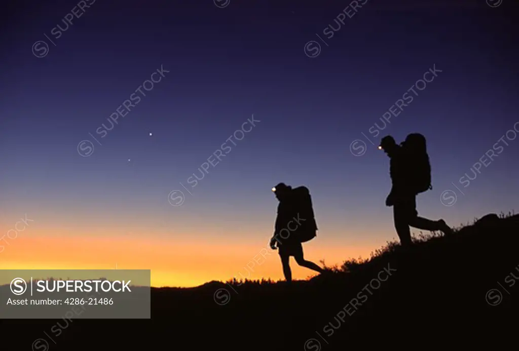 Man and woman silhoutted by the late evening light hike with backpacks and headlamps at Donner Summit, CA.