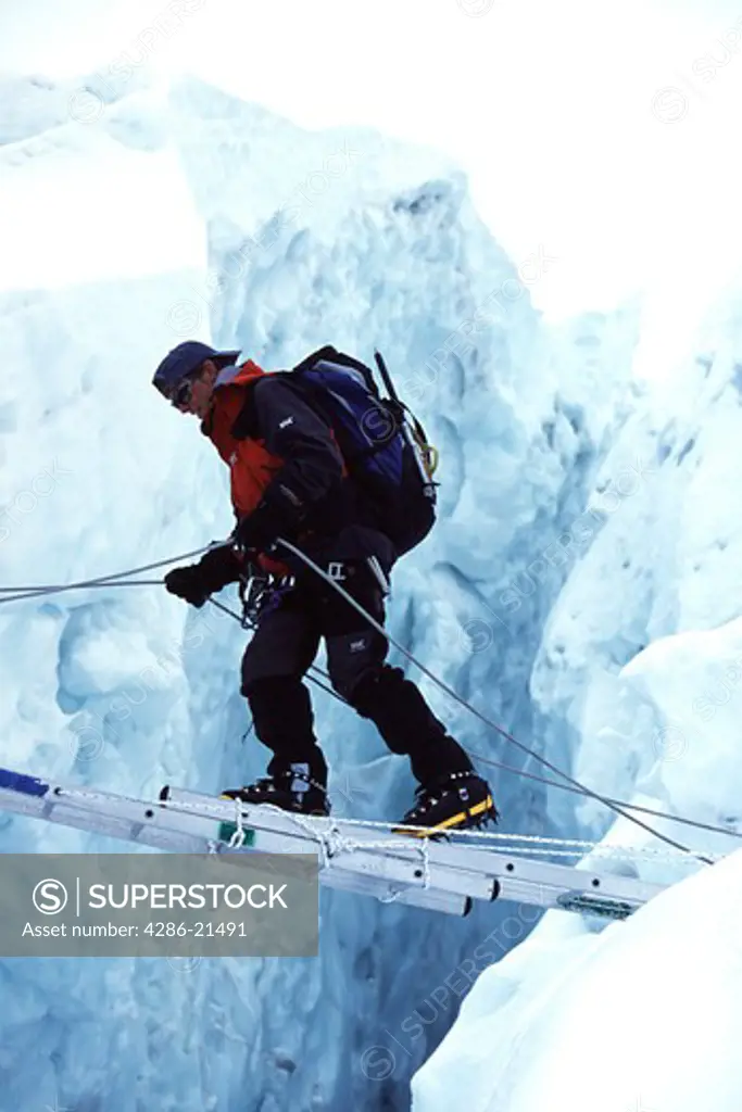 Burdened mountain climber uses a horizontally lying ladder to cross over a crevasse in the Khumbu Icefall region of Mt. Everest.