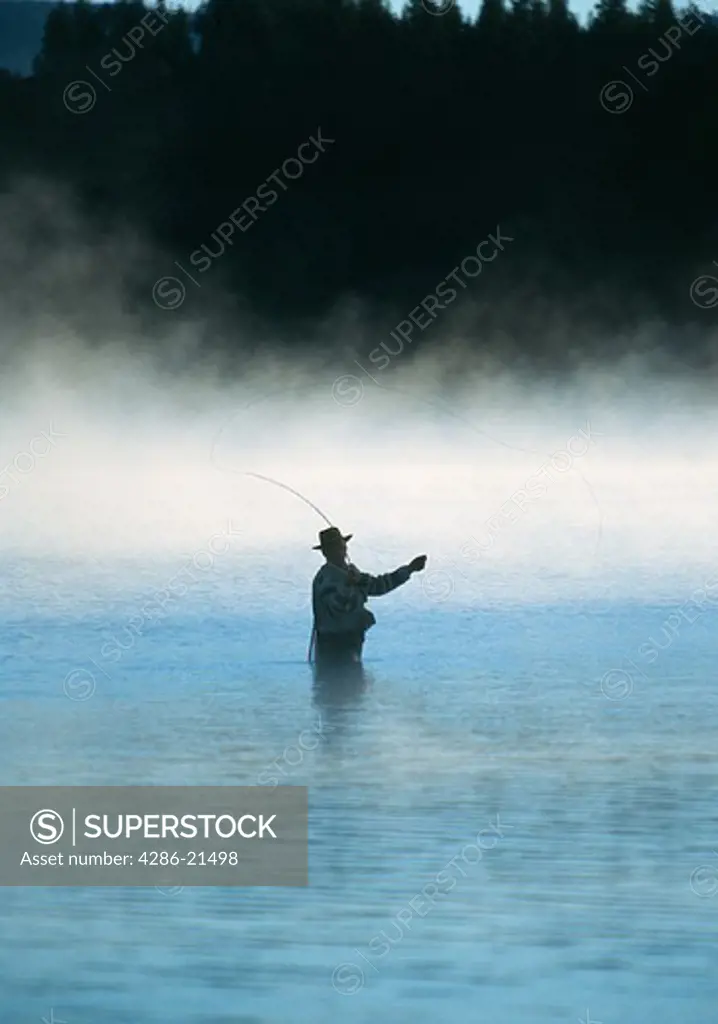 Man stands thigh deep in water as he casts while fly-fishing on a misty day, Stampede Resevoir, CA.