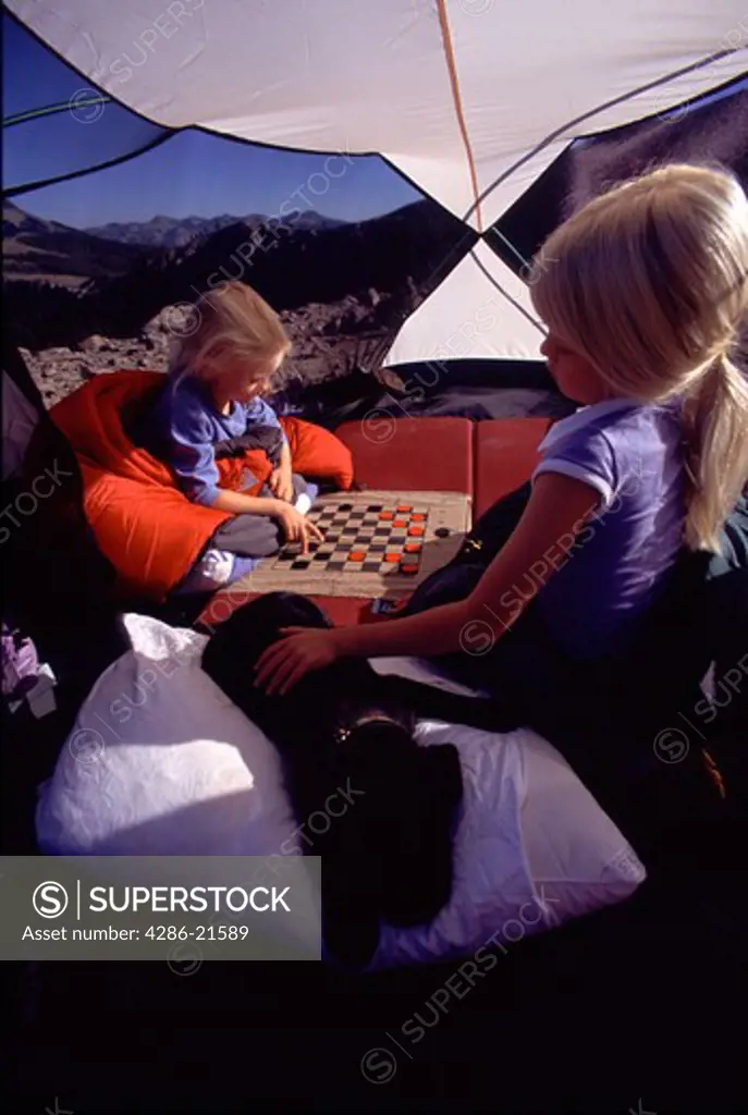 Two sisters and their puppy playing a game of checkers while camping on Mount Judah, CA.