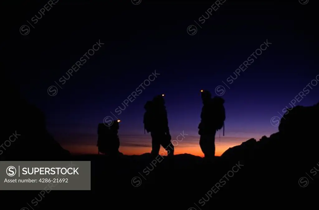 Three mountaineers standing with headlamps glowing on the north ridge of Lone Pine Peak, CA .