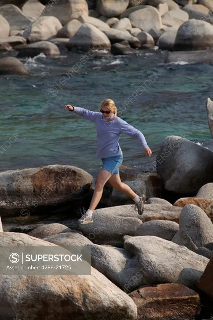 A woman running and rock hopping along the shore of Lake Tahoe, CA.