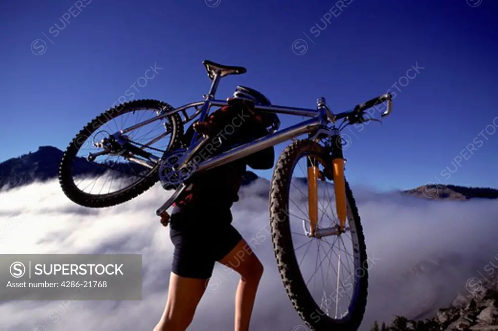 A woman carrying her bike mountain biking above the clouds near Truckee, CA.