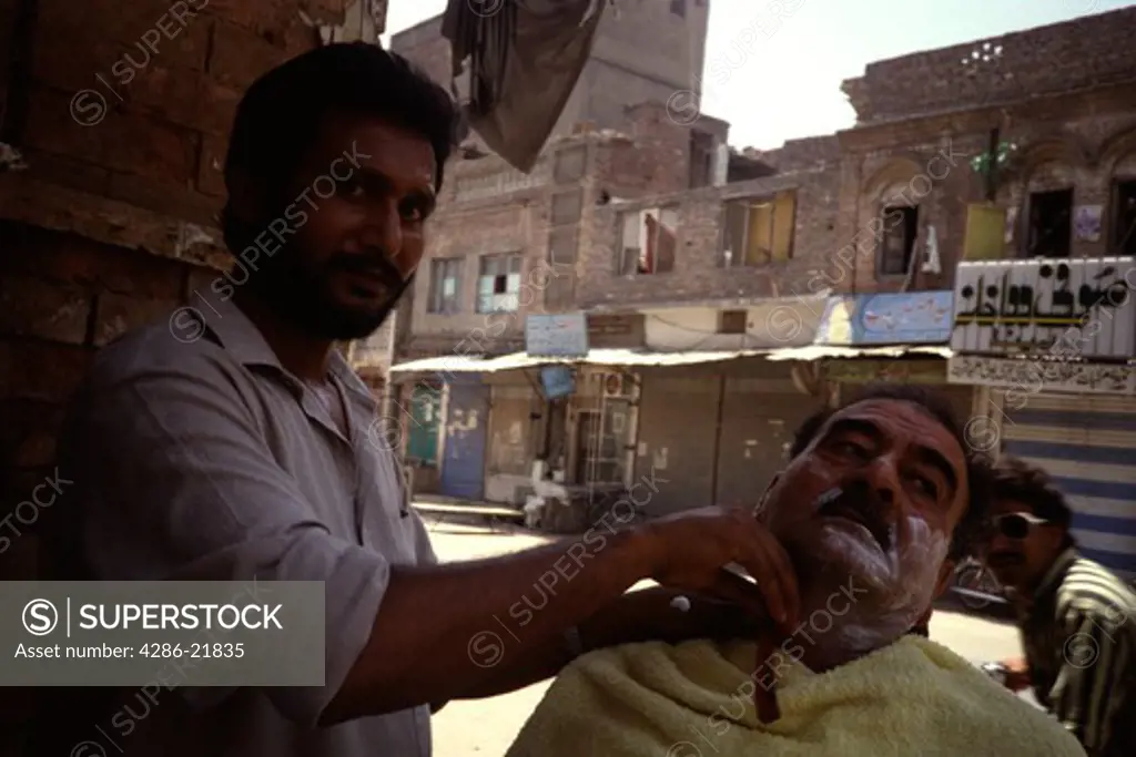 A Pakistani barber shaving a customer on the streets of Rawalpindi.