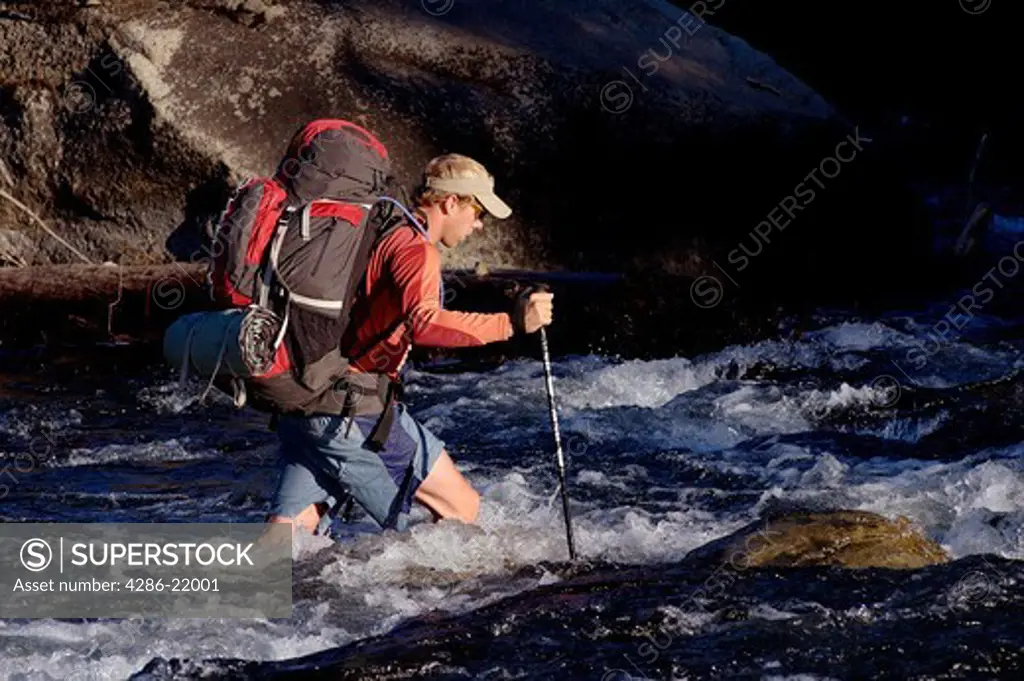 A man crossing a fast river while backpacking near Truckee, CA.