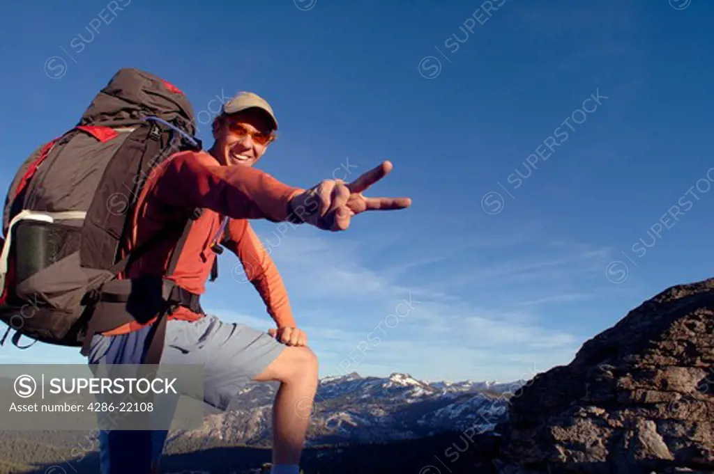 A man celebrating after reaching the summit of a mountain in the Sierras.