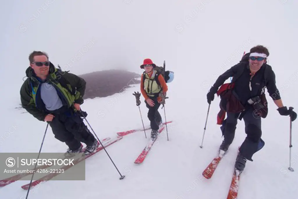 Three skiers climbing Mount Vsevidov in the Aleutian islands on a foggy day.