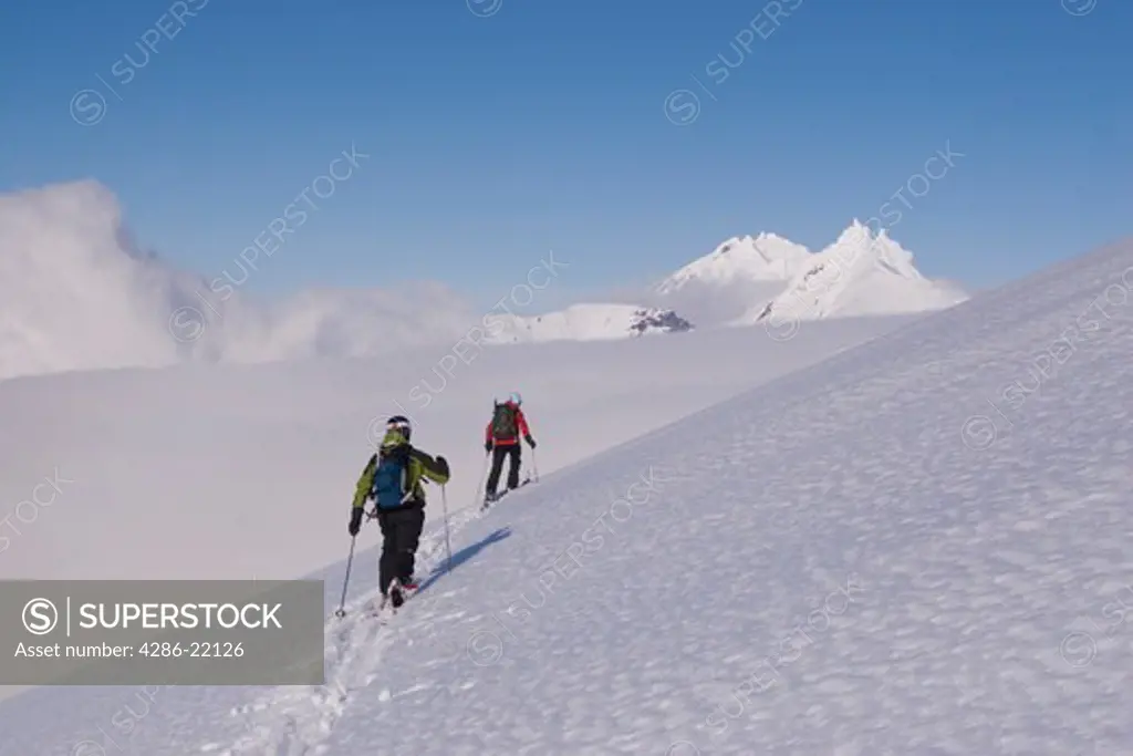 Two ski mountaineers climbing Mt. Vsevidov in the Aleutian islands with Mt. Rechiznoy in the distance.
