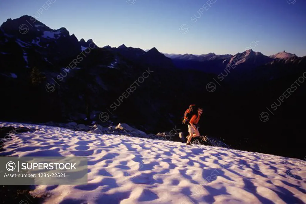 A lone man hiking in summer snow on Maple Pass in the North Cascade mountains in Washington.