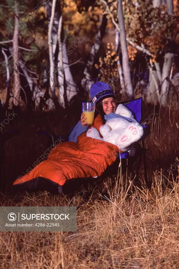 A girl eating breakfast while camping with her bunny rabbit in the fall.