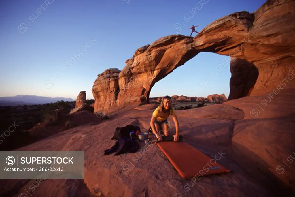 Two people camping next to an arch in Arches National Park, Utah.