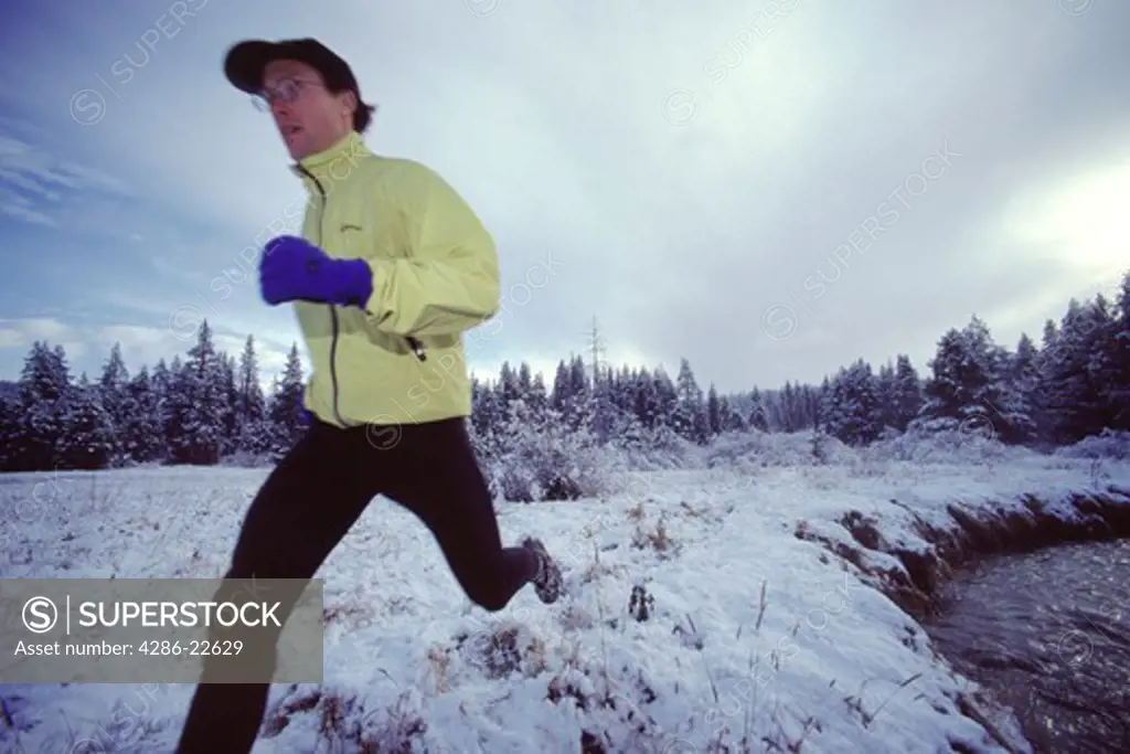 A man running in the snow next to a creek in winter in Truckee, California.