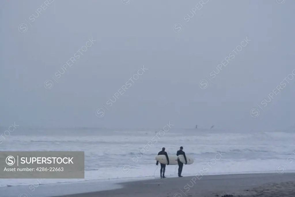 Two surfers walking at dusk along the beach in Oceanside California
