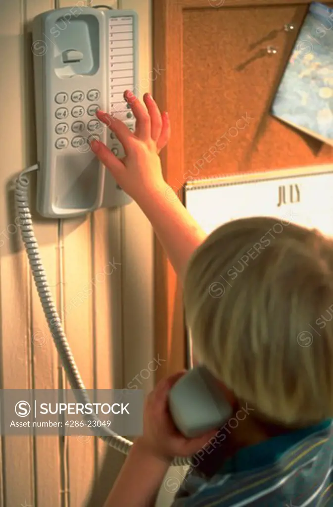 Young 4-year-old boy dialing the telephone in the kitchen of his home.