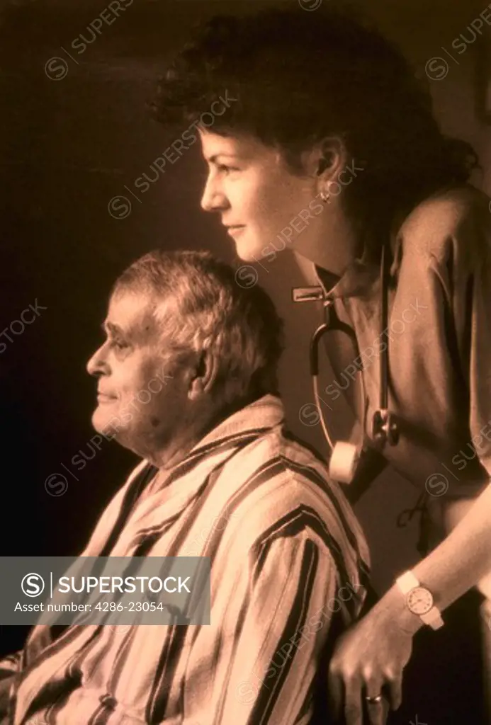 B/W Nurse leans over elderly male patient as she pushes his wheelchair. Beautiful light.
