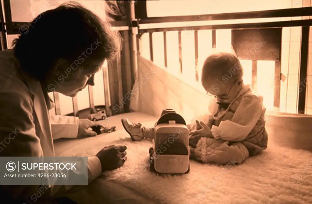 B/W Female doctor examines 1 yo child with vision problem as she sits in her crib.