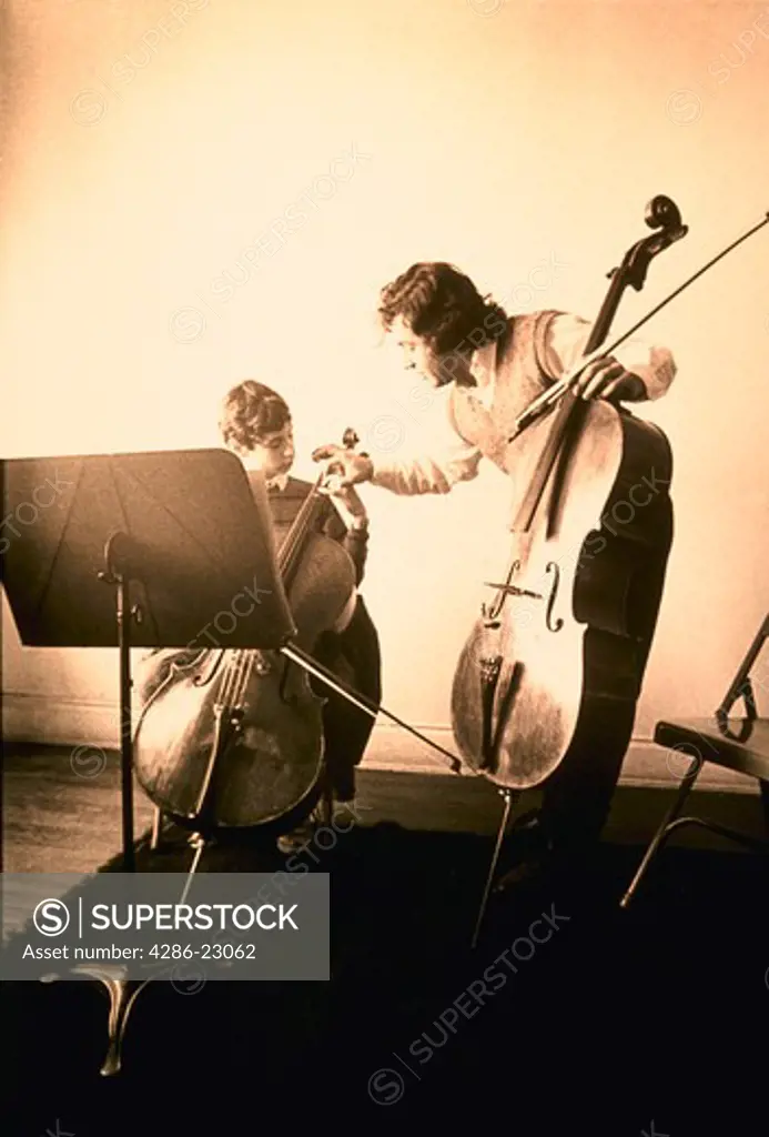Hand colored image of music teacher with cello bending over to fix 12 yo male student's hand as he sits with his cello.
