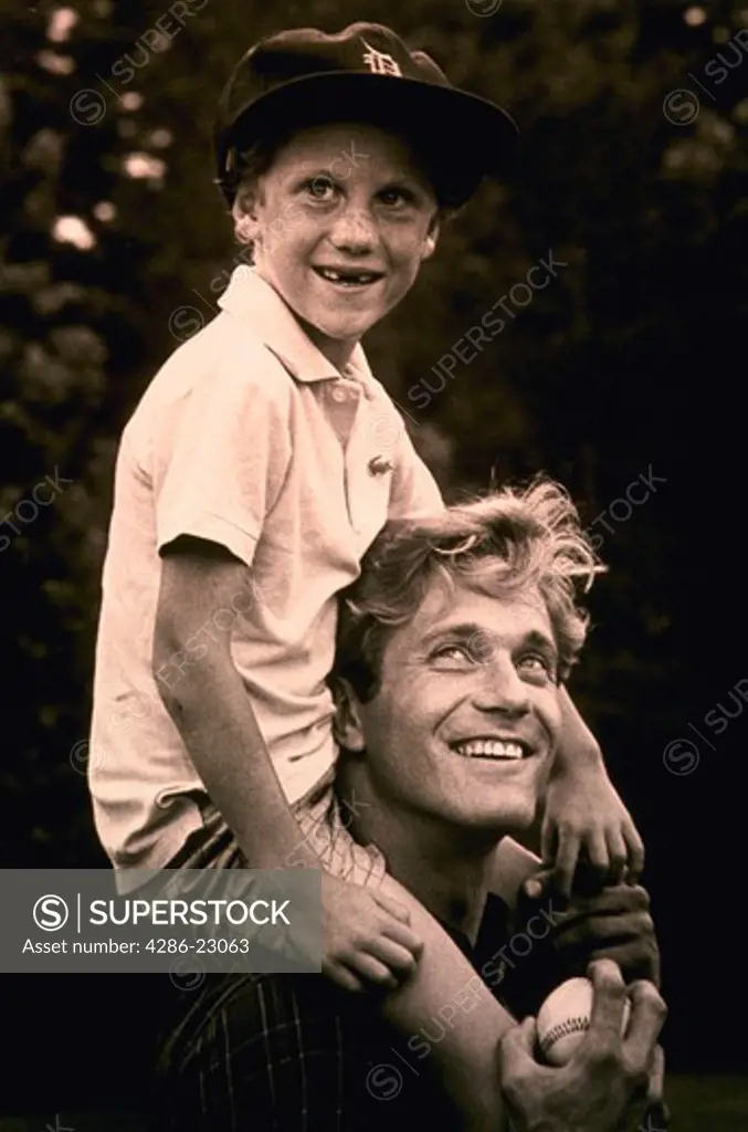 Young boy wearing a baseball cap rides on the shoulders of his father.