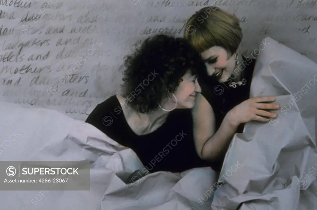  Hand colored portrait of Mother and 20 yo daughter  playing lovingly behind wrinkled seamless with writing in background.
