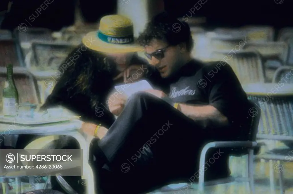 Hand colored image of attractive couple in Venice Italy Having a glass of wine and reading a letter together.
