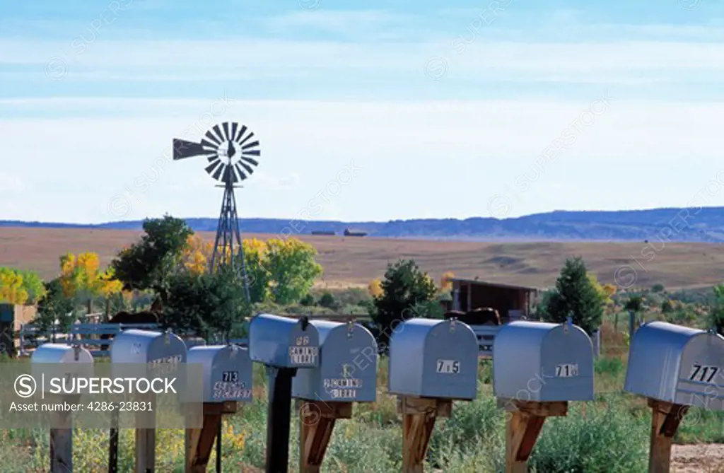 USA, New Mexico. Mail boxes lined up with windmill and open land as a background