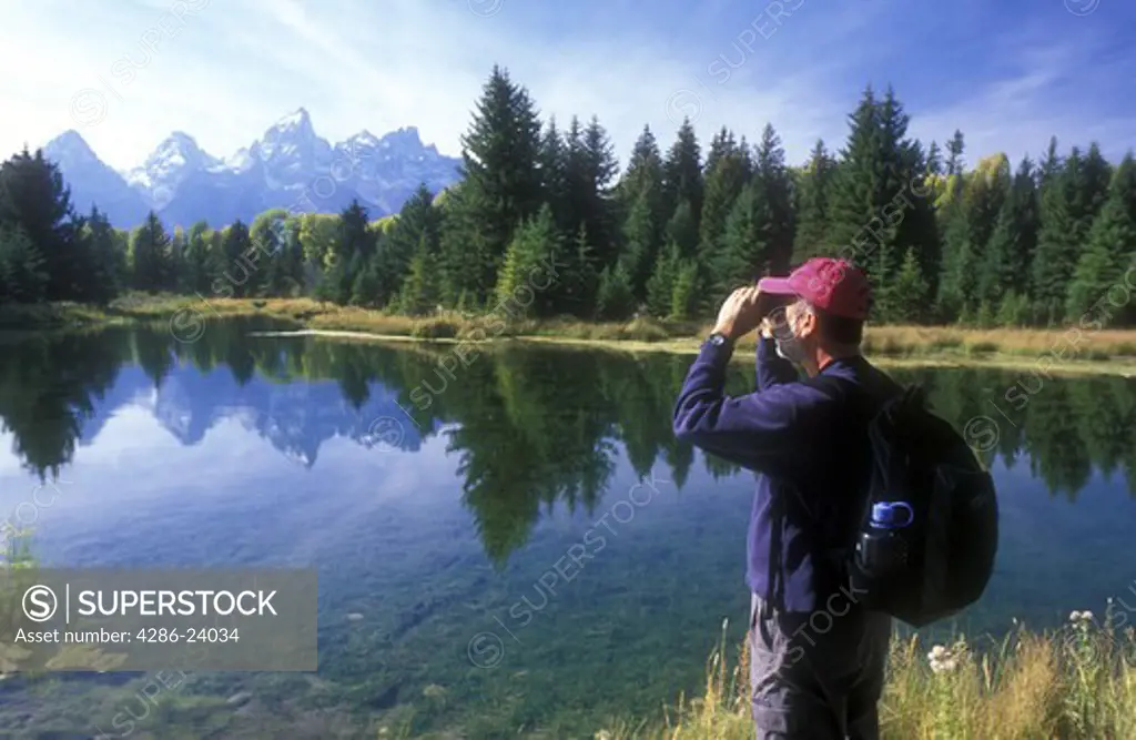 USA, Wyoming, Grand Teton National Park. Reflection of the Grand Teton Mountain Range in a small lake with a 51 year old male looking through binoculars