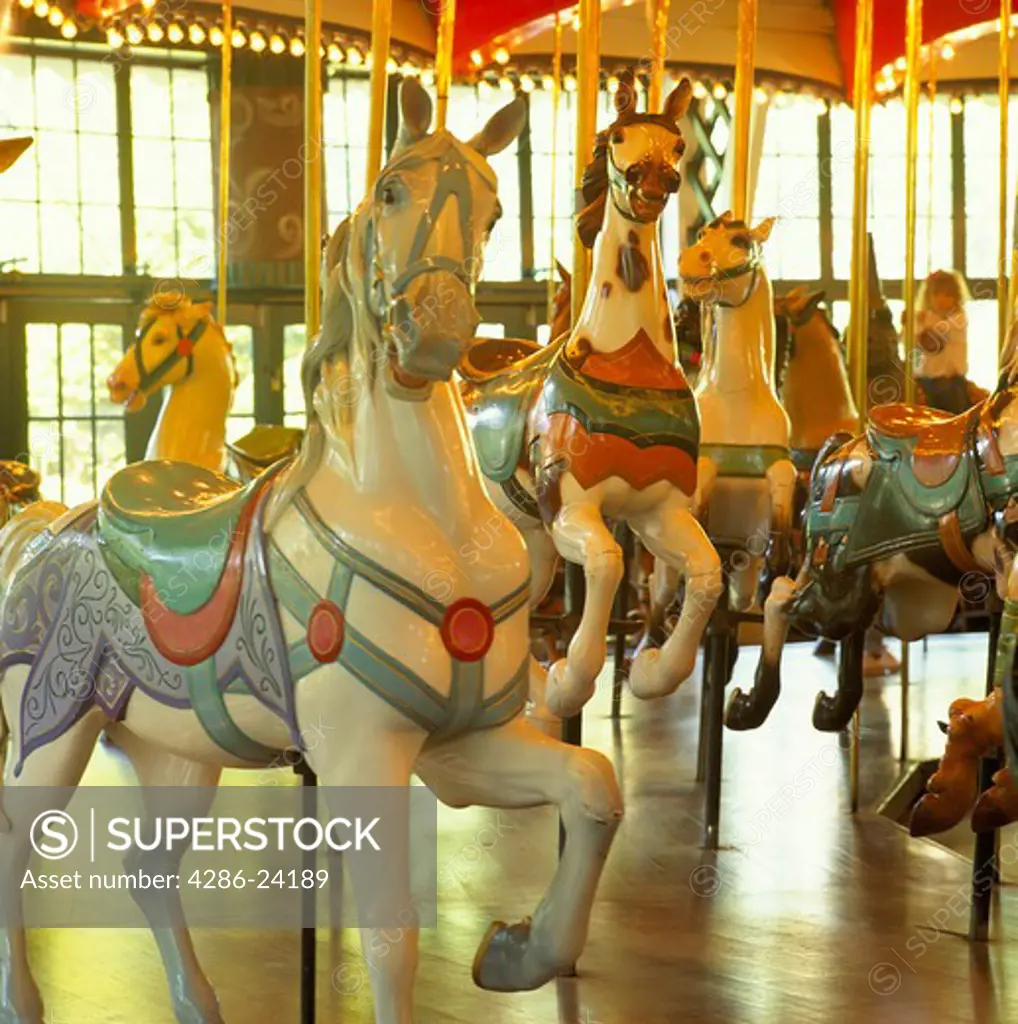 Wooden white merry-go-round horses suspended from shiny brass poles.