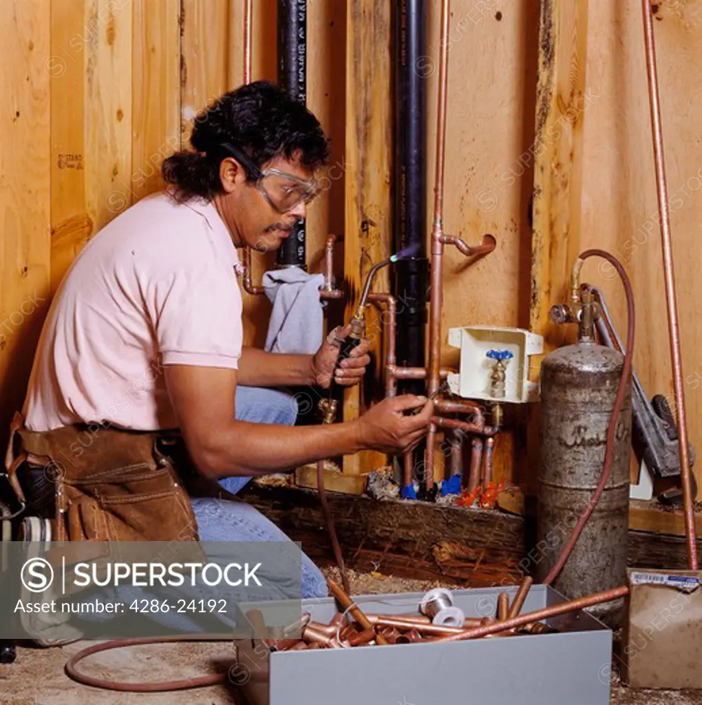 A Latino plumber uses an acetylene torch to solder together copper pipes in the construction of a house.