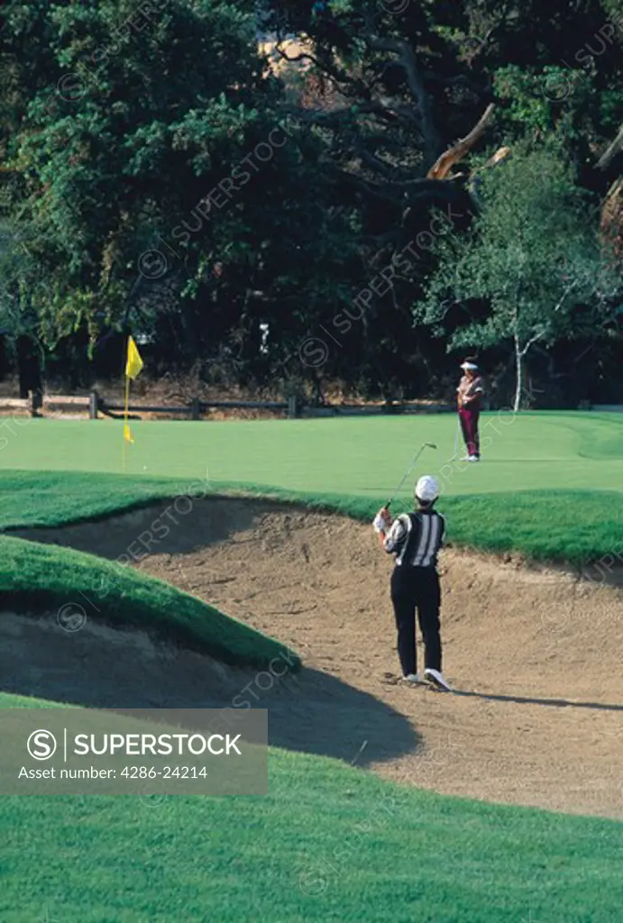 Golfer hitting ball out of a sand trap while his partner watches from the green, Oakhurst Country Club, Clayton, CA