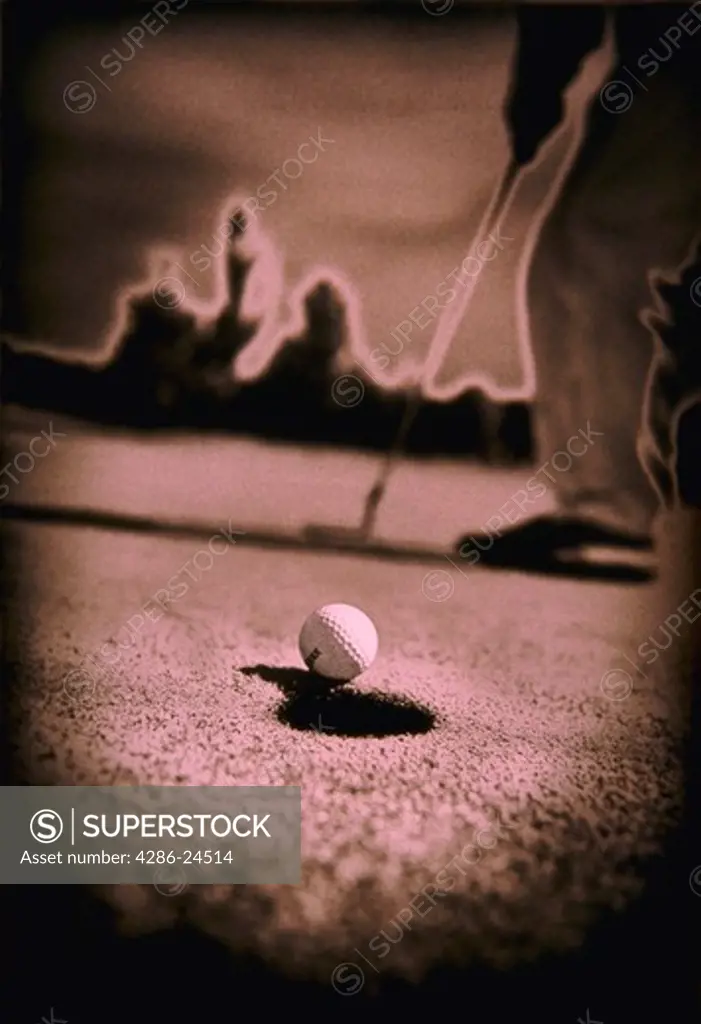 Close-up of golf ball falling into hole with golfer in the background.