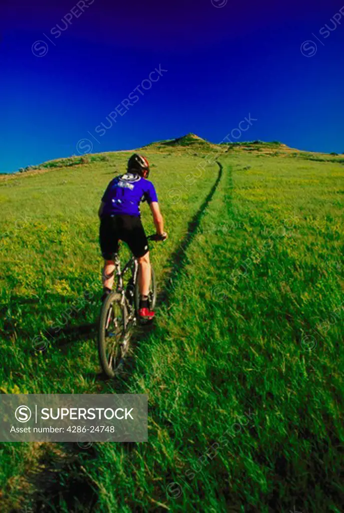 Man riding mountain bike up singletrack, Sully Creek Trail, Little Missouri National Grasslands, North Dakota.