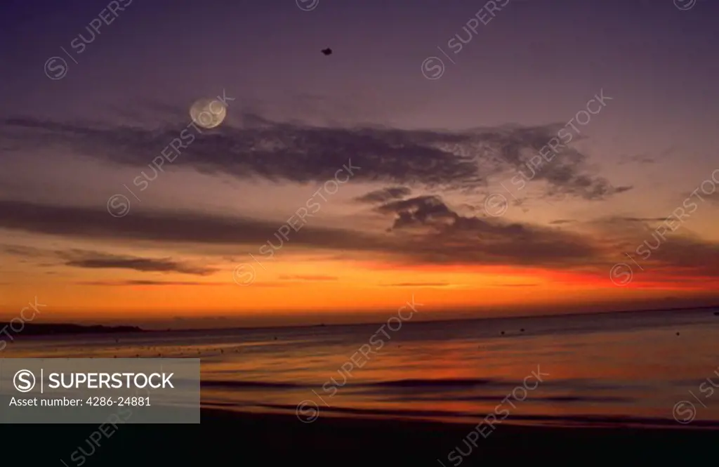 A colorful sunset with a pale moon over Seven Mile Beach in Negril, Jamaica.