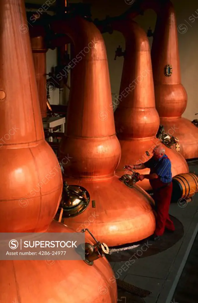 Copper whiskey stills and stillman at distillery in Scotland.