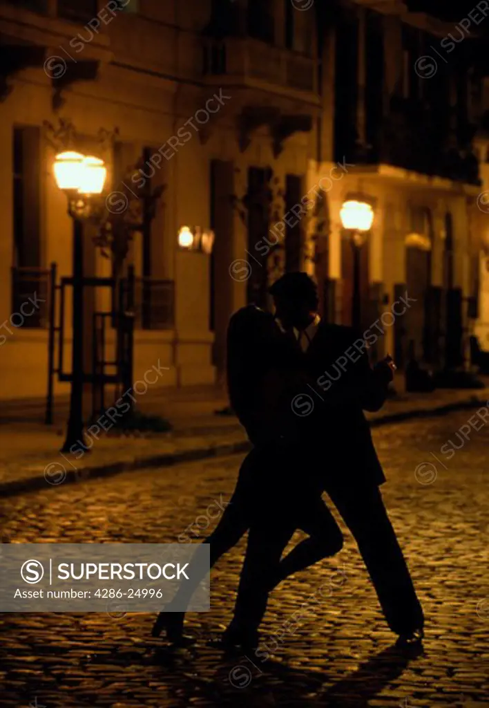 Couple passionately dancing the tango among streetlights on a cobblestone street in San Telmo, Buenos Aires, Argentina.