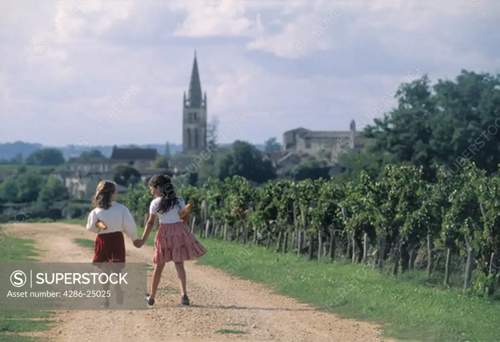 Two school girls walking through vineyards with baguettes near village of St Emilion in France 