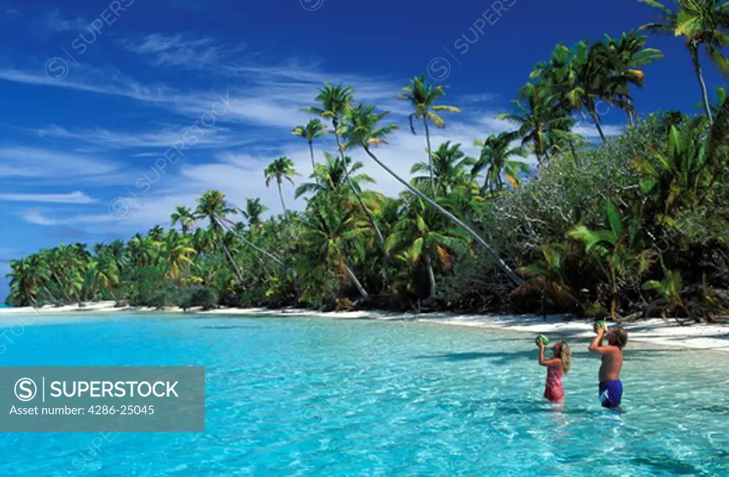 Couple drinking from coconuts on palmtree lined beach off One Foot Island near Aitutaki in Cook Islands South Pacific