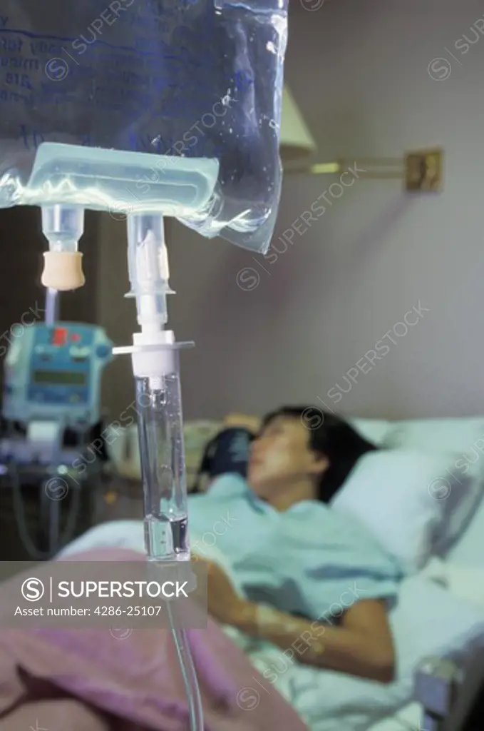 Woman connected by IVs to fluids in hospital recovery room bed