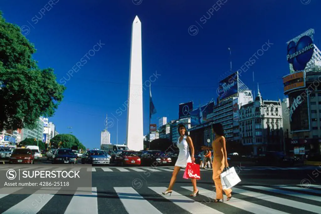 Two women crossing Avenida 9 de Julio in Buenos Aires with shopping bags and Obelisk behind