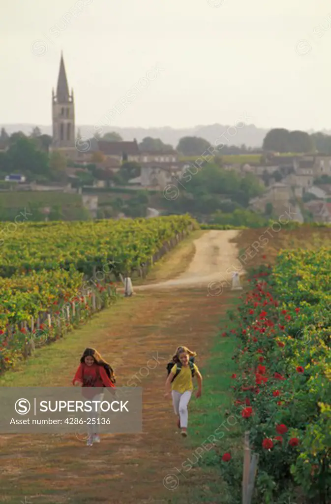 Two school girls running through vineyards near village of St Emilion in France 