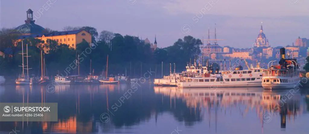 Boats and skyline reflecting on glassy Nybroviken waters in Stockholm at sunrise