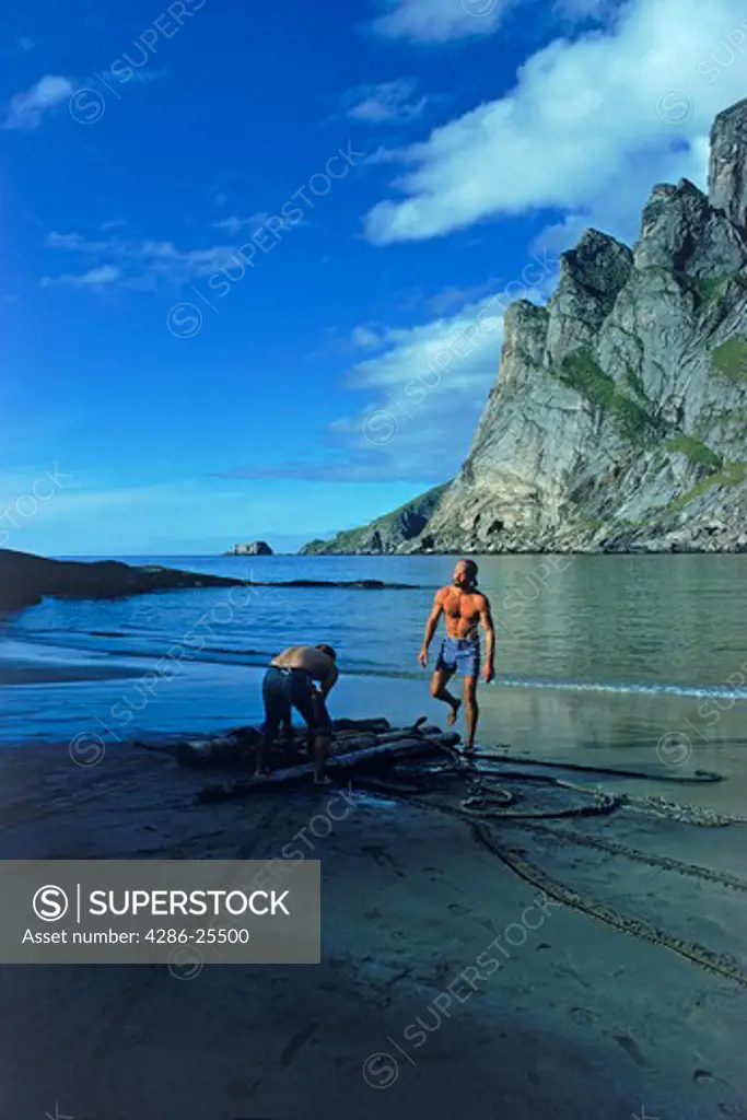 Two hikers building makeshift raft from driftwood in Lofoten Islands