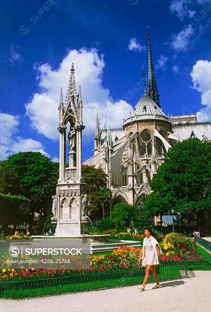 Woman passing gardens on Ile de la Cite with Notre Dame in Paris